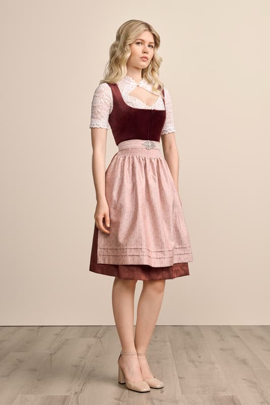 Das Samtdirndl Aurela ist ein wahrhaftiger Hingucker! Das unifarbene Mieder aus edlem Samt betont ein elegantes Dekolleté durch den gerade Ausschnitt. Der Rock ist mit einem wunderschönen zart schimmernden Muster verziert und bringt Eleganz in das Outfit. Das Dirndl wird vorne mit einem praktischen Reißverschluss geschlossen. Abgerundet wird der Look durch eine stilvolle Schürze mit einem tollen Ornamentmuster. Mit einer Rocklänge von 60 cm